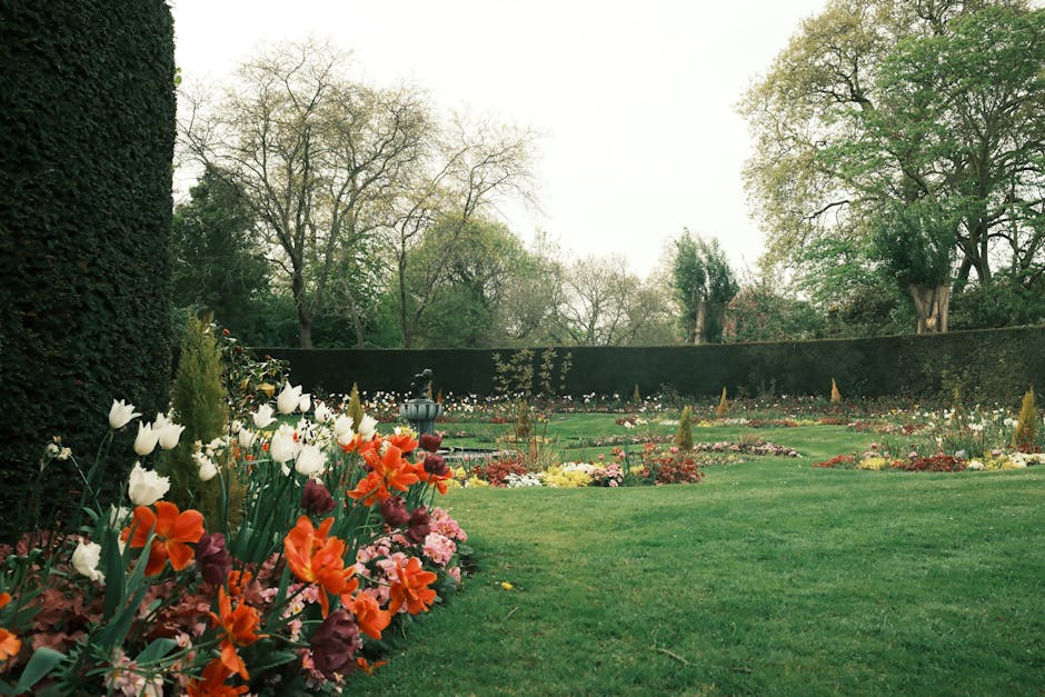 A well-maintained garden in Brockwell Park with a neatly trimmed lawn bordered by vibrant flower beds containing a mix of tulips, daffodils, and other seasonal blooms. The flower beds are edged with r